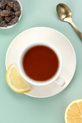 A teapot, a cup of black tea in a white ceramic mug with lemon, sugar and a spoon on a green background. Top view.