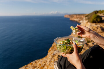 Woman eating a salad on a cliff with a beautiful seascape