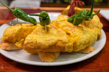 Typical snack of Basque Country, pinchos or pinxtos, small piece of bread with egg omelette, different toppings, served in bar in San-Sebastian or Bilbao, Spain