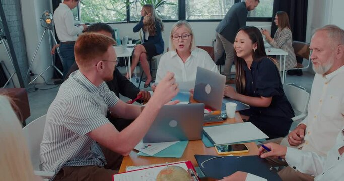 Beautiful happy middle aged female leader, company boss works together with multiethnic team at light office slow motion