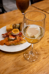 Board with typical snacks of Basque Country, pinchos or pinxtos, skewers or small piece of bread with toppings, served with glass of txakoli wine in bar in San-Sebastian or Bilbao, Spain