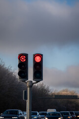 Traffic light showing red lights and left arrow with traffic behind against cloudy sky