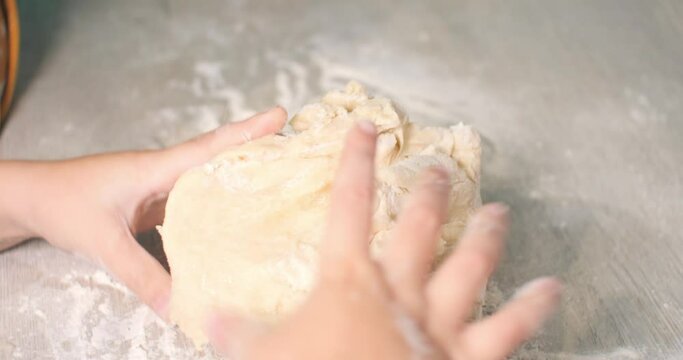 Children's hands help mom knead the dough. The child takes out a lump of dough from the mix and starts kneading it on the kitchen table. The family prepares dough for baking.