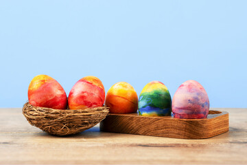 Colorful Easter eggs in a wooden egg stand and a decorative nest of sisal on a blue background with a place for text. Happy Easter concept. Greeting card.