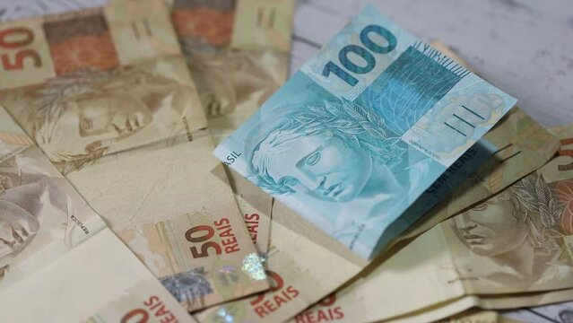 Notas do Real Brasileiro sobre uma mesa de madeira. Nota de 100 Reais sendo movida pelo vento. Economia brasileira e finan&ccedil;as.
