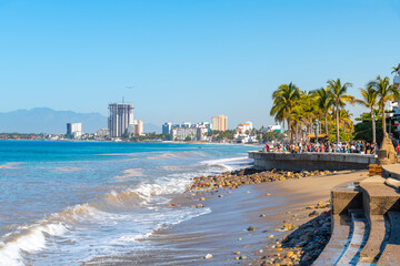 Fototapeta na wymiar The sandy beach alongside the Malecon promenade boardwalk and Zona Romantica area of Puerto Vallarta, Mexico, with the sea and city skyline in view.