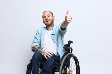 A man in a wheelchair looks at the camera shows a thumbs up, happiness, with tattoos on his hands...