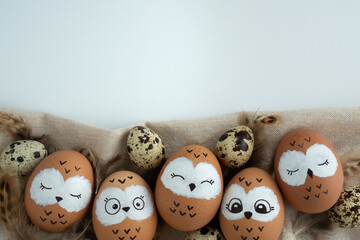 Funny owl family. Brown easter eggs with painted faces, quail eggs and bird feathers. Space for your text.