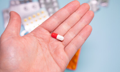 Male hand holding a pill against blue background.
