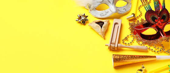 Hamantaschen cookie, carnival masks and noisemakers for Purim holiday on yellow background with space for text