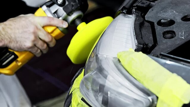 Caucasian man polishing headlights of a car using yellow polisher.