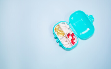 Plastic box with different pills on light blue background, top view. 