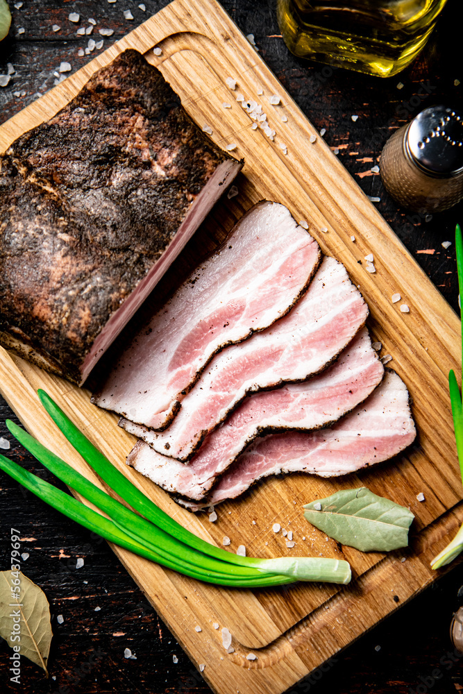 Poster Pieces of pork lard on a cutting board with green onions and bay leaves. 