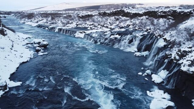Waterfall in Iceland, Snowy Mountain with Cold River in Winter, Magical Winter Time Location, Blue Glacial Water with a Huge Current. Pure Scenic Landscape. Hraunfossar. 
