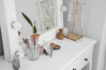 Table with cosmetics, brushes, jewelry and mirror in makeup room
