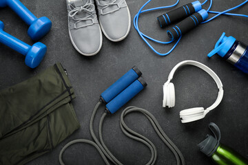 Skipping ropes with dumbbells, bottles, headphones, sneakers and clothes on dark background