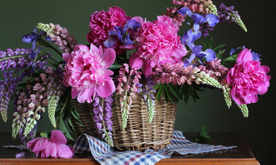 a bouquet of peonies, lupines and irises in a basket indoors.