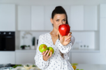 a beautiful European brown-haired girl stands in a white kitchen in a beautiful dress with polka dots and holds apples in her hands. Focus, kitchen concept, healthy food, confectioner, nutritionist