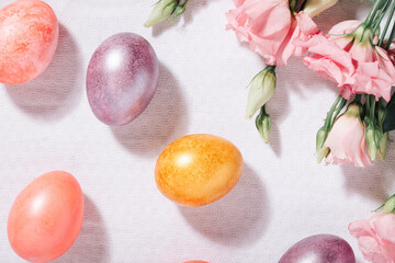 Obraz na płótnie Canvas Gold, purple and pink painted Easter eggs in pastel colors and flowers on a white cotton tablecloth top view