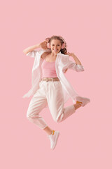 Young woman in headphones dancing on pink background