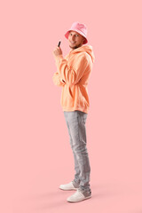 Young man in bucket hat with disposable electronic cigarette on pink background