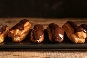 Plate with tasty chocolate eclairs on dark wooden table, closeup