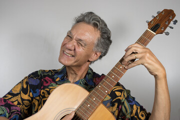 Senior man wearing a colorful shirt playing his acoustic guitar 