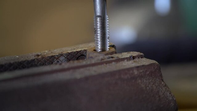 Close up worker cuts the damaged thread of a nut bolt clamped in a vise. Steel cutting tool when working thread on metal nut bolt