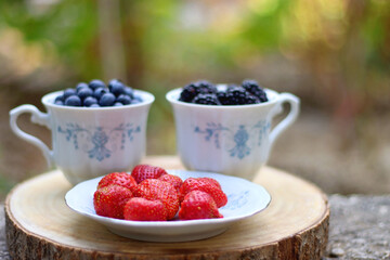 Blueberries, blackberries and strawberries in the vintage porcelain set. Healthy snack served in a garden. Selective focus.