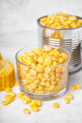 Bowl with corn kernels, tin can and cobs on white table