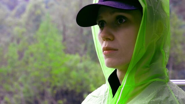 Unhappy woman hiker in yellow raincoat hide from rain in forest, failed trekking