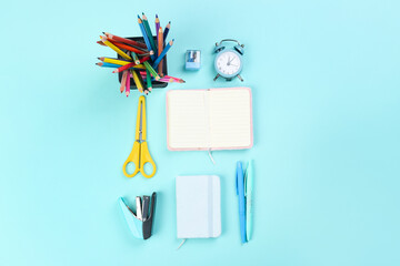 Holder with stationery, notebooks and alarm clock on blue background