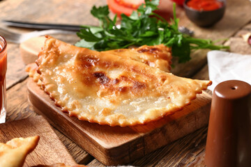 Cutting board with tasty chebureks on wooden background