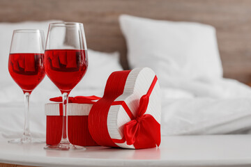 Glasses of wine and gifts for Valentine's Day on table in bedroom, closeup