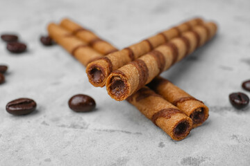 Delicious rolled wafer cookies and coffee beans on grunge background, closeup