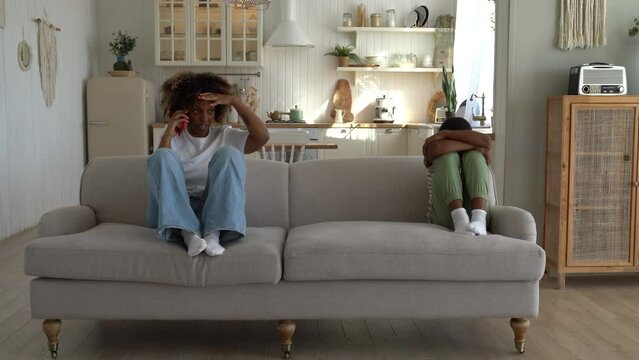 Disappointed by bad child behavior mother talking on phone while sitting on sofa at home with upset crying son. Stressed parent mom making call complaining about naughty kid. Parenting problems 