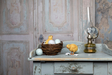 Easter still life on vintage wooden blue table with an old kerosene lamp, bird nest, easter eggs and yellow chicks on an old palace door background