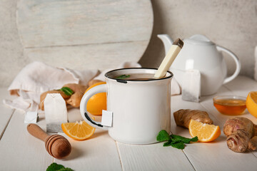 Cup of tea with mint, ginger, spoon, teapot and lemon on light wooden background