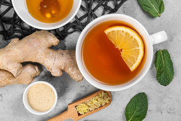 Cup of black tea with lemon, ginger roots, honey and mint leaves on grey table