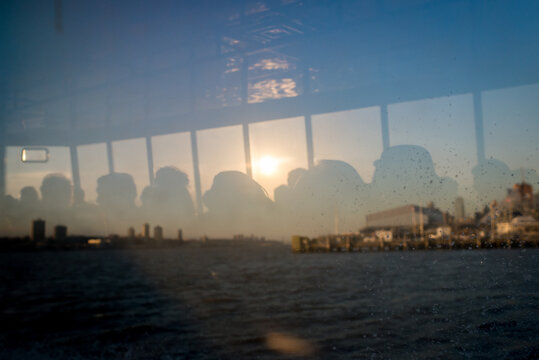 Silhouette of commuters reflecting on farry boat window during sunset