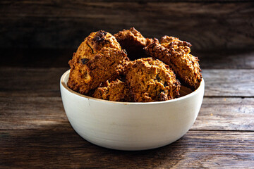 Homemade oatmeal cookies in a white bowl on a kitchen wooden table.