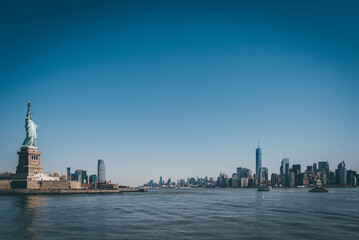 Fototapeta na wymiar Statue of Liberty in front of NY skyline and blue skies