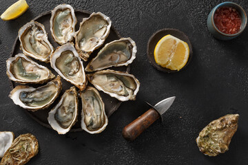 Huîtres fraiches, ouvertes dans une assiette avec des glaçons et citron sur un fond noir. Fruits de mer. Vue de dessus. 