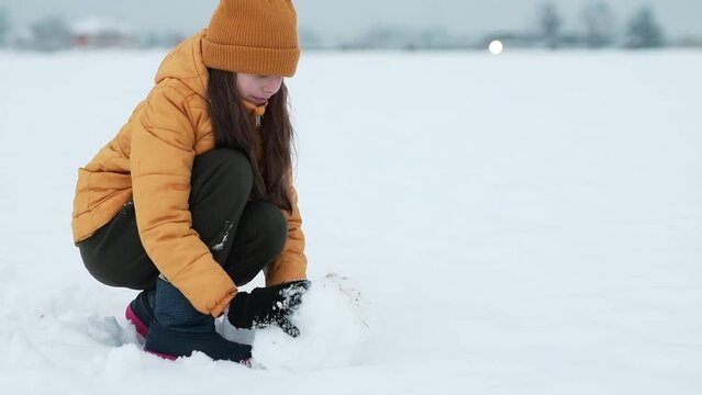 A happy teenager enjoying the snowfall. Girl making a snowman outdoors