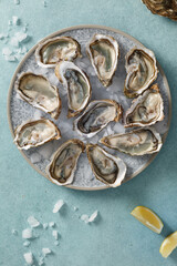 Huîtres fraiches, ouvertes dans une assiette avec des glaçons et citron sur un fond bleu. Fruits de mer. Vue de dessus. 