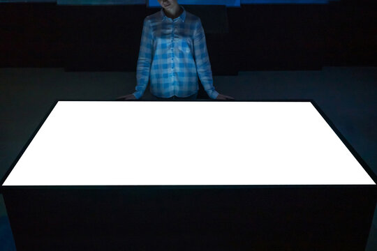 Mock up, copyspace, template, education, future and technology concept - woman looking at white blank interactive touchscreen display table kiosk in dark room of modern technology museum