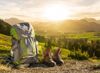 Hiking equipment in sunset sunlight and mountain silhouettes. Backpack and boots in beautiful sunlight. Allgaeu, Bavaria, Alps, Germany.
