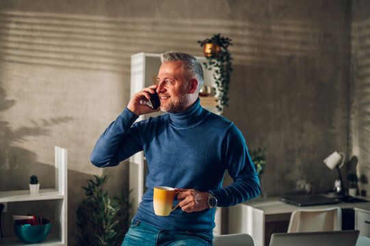 Middle aged man using smartphone and drinking coffee at home
