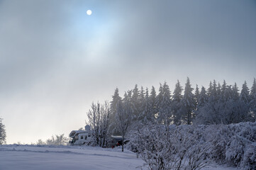 Sun barely visible through clouds in snow landscape with a mobile home or camper