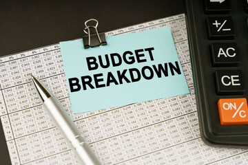 On financial reports lies a calculator, a pen and a sticker with the inscription - BUDGET BREAKDOWN